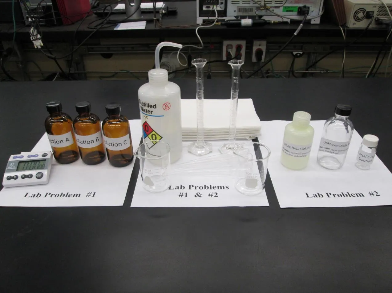 2016 USNCO Part III lab setup showing three zones: Problem 1 (Solutions A, B, C + timer), shared equipment (distilled water, flasks), Problem 2 (unknown acid)