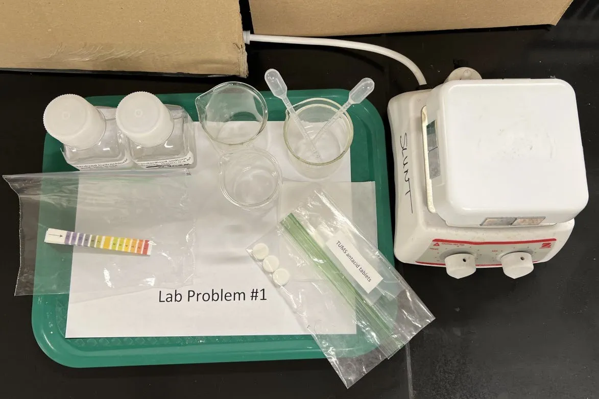 2022 USNCO Part III Problem 1 setup: pH indicator strips, antacid tablets, beakers, pipets, balance on green tray